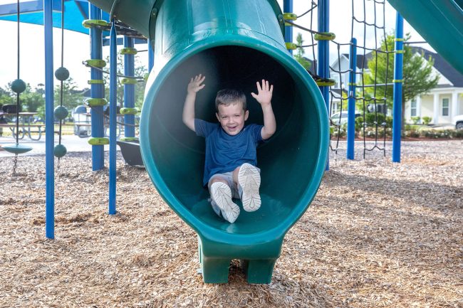 A young boy emerging from a tube slide on the playground