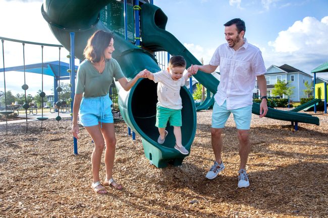Parents holding son's hands as he's emerging from a tube slide