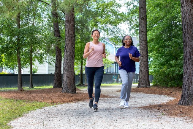 Two women jog on a gravel path through trees